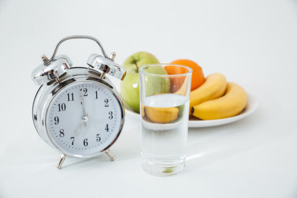 zegar obok talerza z owocami i szklanką wody
